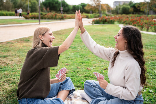 Friends high five after a card game on a park picnic