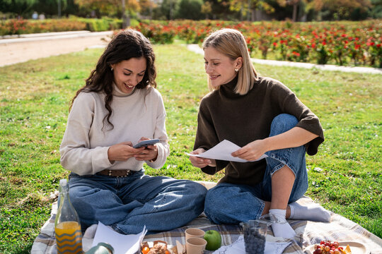 Two women planning a park picnic with paper and phone