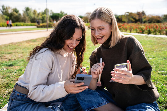Two young women watching makeup tutorial on phone outside