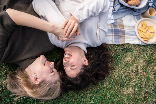 Couple laughing on picnic blanket in park holding hands