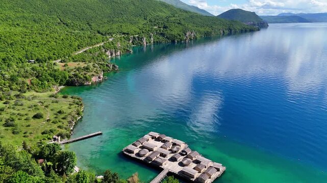 Aerial view of the Bay of Bones Museum on Lake Ohrid, North Macedonia. Crystal-clear turquoise water and lush green mountains create a stunning landscape. 