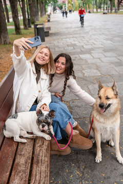 Two women taking selfie with dogs on park bench