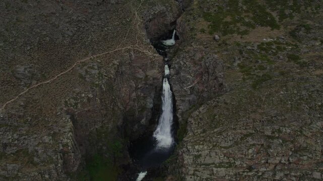 Drone footage of Kurkure waterfall flowing into a dark pool between steep rocky cliffs and mountain tundra, Altai Republic, Russia, remote wilderness landscape