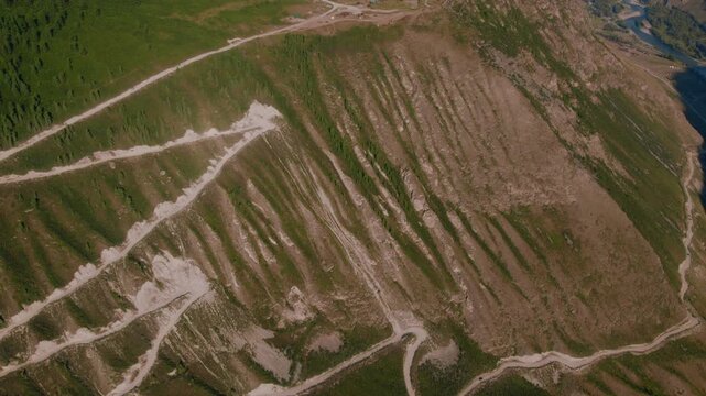 Drone footage of the steep serpentine dirt road descending Katu-Yaryk Pass above a deep green valley in the Altai Mountains, Altai Republic, Russia