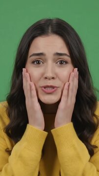 Young woman looking at camera with shocked and surprised face expression on green screen.