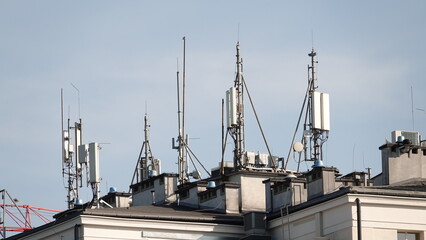 Nowoczesne anteny telekomunikacyjne i nadajniki sieci komórkowej zamontowane na dachu budynku mieszkalnego w przestrzeni miejskiej na tle bezchmurnego nieba w słoneczny dzień © tomo81