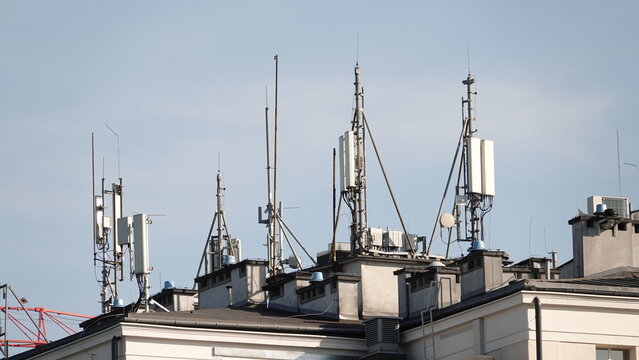Nowoczesne anteny telekomunikacyjne i nadajniki sieci kom&oacute;rkowej zamontowane na dachu budynku mieszkalnego w przestrzeni miejskiej na tle bezchmurnego nieba w słoneczny dzień