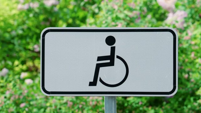 Wheelchair accessibility sign displayed outdoors against a background of green plants and flowers