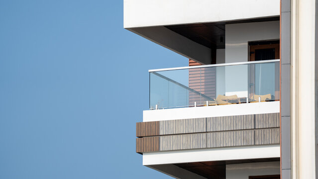 Modern apartment building corner balcony with glass railing and wood cladding against blue sky