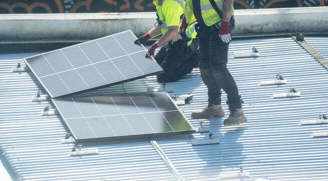 Two worker in yellow vest installing solar panel on metal rooftop surface