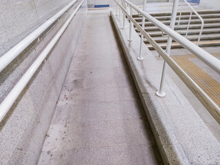 Obraz premium Stone accessibility ramp with white metal handrails next to stairs. Public facility infrastructure with yellow tactile paving