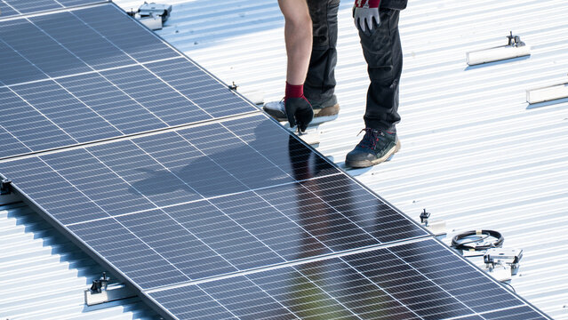 Worker standing beside installed solar panel row on flat metal rooftop surface
