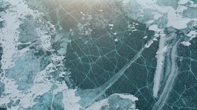 Top view aerial footage of winter ice with natural cracks, bubbles and snow patches on Lake Baikal, Irkutsk Oblast, Russia, cold seasonal background texture