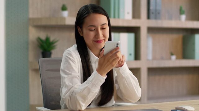 Happy Chinese businesswoman talking mobile phone recording voice message office worker Korean Asian Japanese girl business woman female manager use smartphone online call speakerphone send SMS indoors