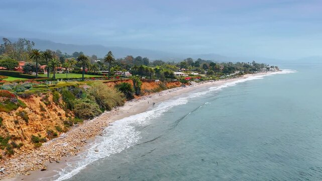 Sportsmen are paddle-boarding near the coast of Santa Barbara, California, USA. Picturesque shore of American Riviera with lush greenery.