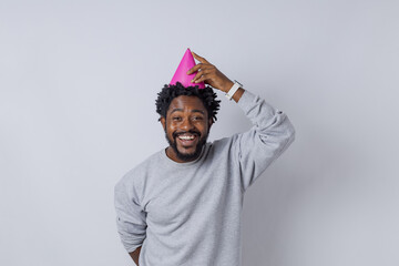 Fototapeta premium happy Handsome black man, wearing gray tracksuit and a pink birthday hat, against an infinity background. White photography studio. Rio de Janeiro, Brazil.