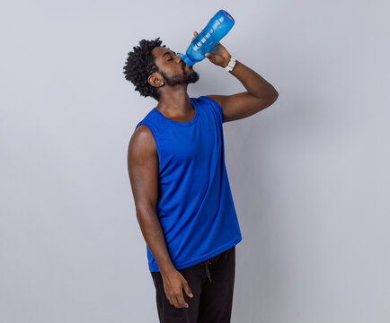 Black man wearing a blue shirt against a white background, drinking water. White photography studio. Rio de Janeiro, Brazil.