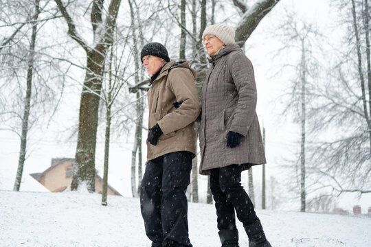 Elderly couple strolling at unhurried pace with a house in the distance sharing comfortable companionship. Mature man and woman near their home and belonging. Cozy peaceful residents on a winter walk