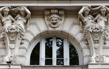 Stunning architectural detail of a classical Parisian building facade featuring two elegant female atlantes in draped robes raising their arms to support an entablature, flanking an arched window. © kovalenkovpetr
