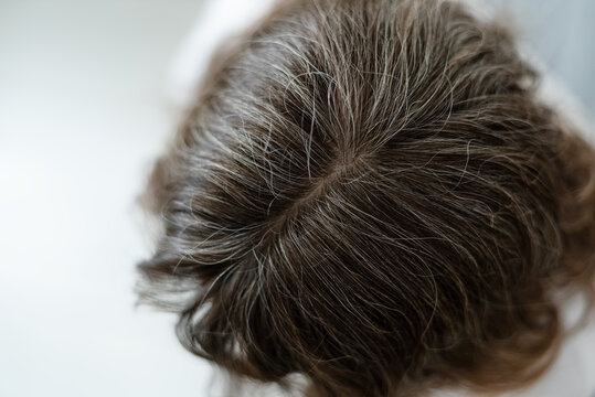 A woman observes how period of high stress has caused her hair to turn gray. The mature adult sees physical evidence of emotional pressure in silver strands. Mother links anxiety to aging.