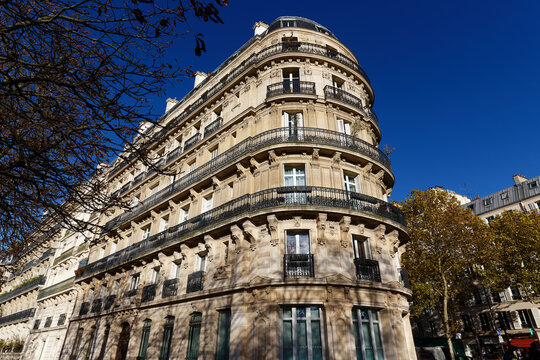 Majestic curved corner apartment building on Avenue de l'Observatoire in the 6th arrondissement of Paris, photographed under a deep cobalt blue sky in autumn. 
