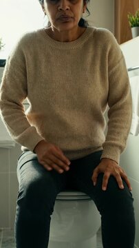 Mature Indian woman sitting on toilet suffering from severe stomach pain. Constipation, food poisoning, UTI or irritable bowel syndrome concept
