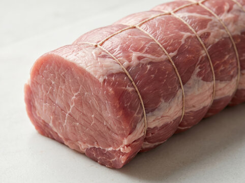 Raw pork loin tied with butcher twine on a marble surface