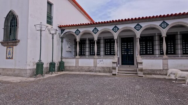 Traditional Portuguese church architecture featuring a stone paved courtyard under bright daylight with arched arcades decorative iron street lamps and white walls