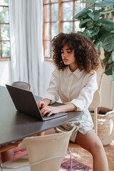 Fototapeta premium Young woman typing on laptop while seated at dining table