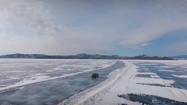 Drone footage of a vehicle driving on an ice road across frozen Lake Baikal in winter, surrounded by snow and blue ice with distant mountains, Siberia, Russia