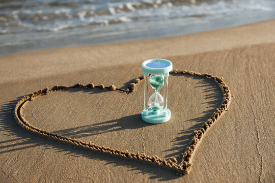 Hourglass on sandy beach inside heart shape