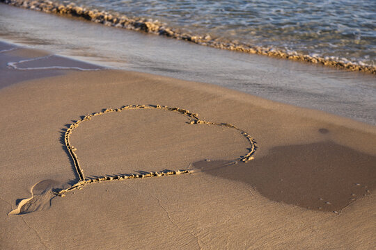 Heart drawn in sand on a sunny beach at sunset