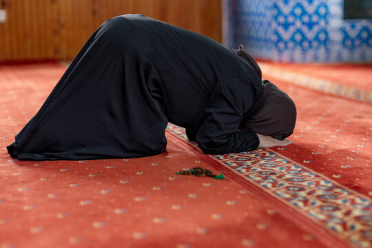 Muslim woman praying in mosque during salah on carpet