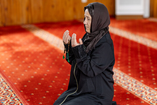 Muslim woman praying with tasbih on mosque carpet indoors
