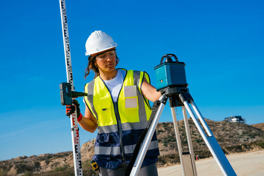 Female construction surveyor in helmet using tripod level