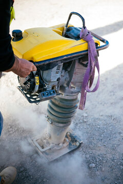 Worker using vibration rammer compactor on road base