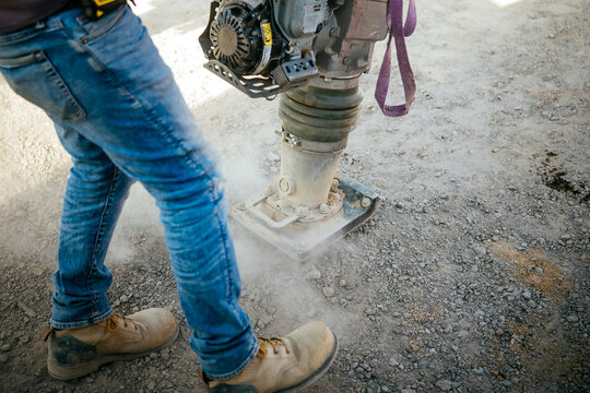Construction worker using plate compactor on gravel ground