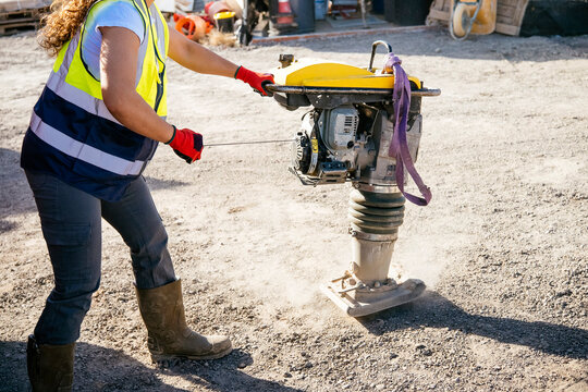 Female construction worker operating compactor on gravel site