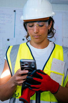 Female construction worker using phone with helmet and PPE