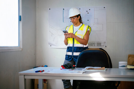 Female construction worker in helmet using phone in office