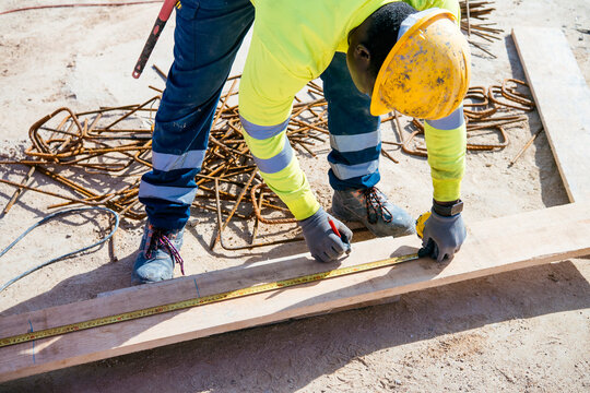 Construction worker measuring and marking wood plank on site