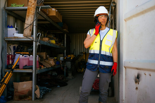 Female construction worker in safety gear using phone on site