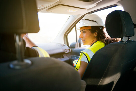 Female construction worker wearing hard hat riding in car
