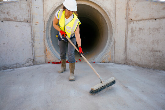 Construction worker woman sweeping concrete drainage tunnel