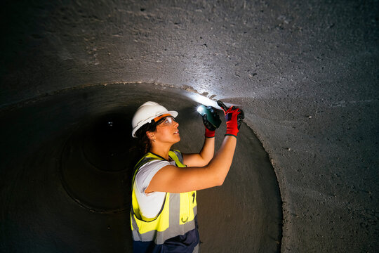 Female construction worker inspecting concrete tunnel with light