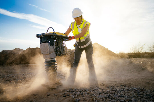 Female construction worker using compactor at dusty site