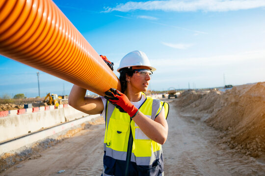 Female construction worker carrying pipe at roadwork site
