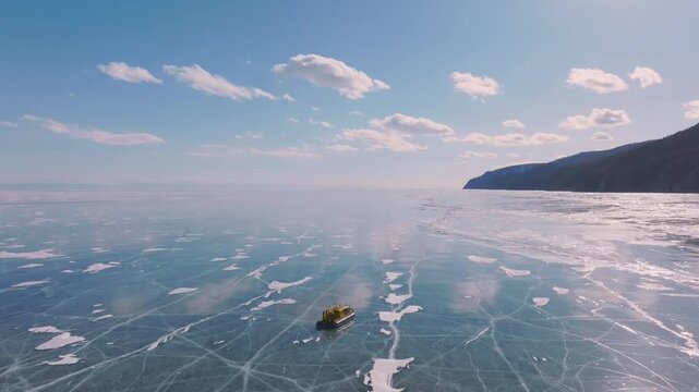 Aerial footage of a hovercraft khivus driving across cracked blue ice on Lake Baikal in winter, Irkutsk Oblast, Russia, with mountains on the horizon