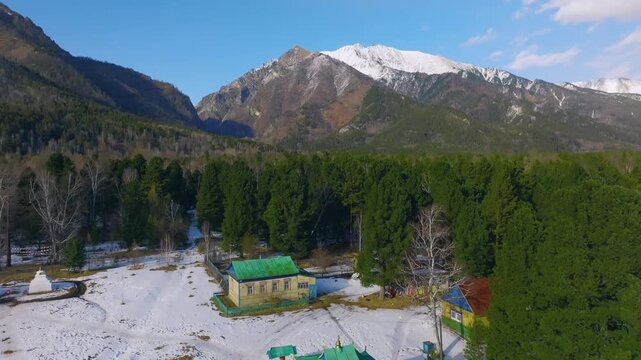 Drone footage of Khoimorsky Datsan Buddhist temple complex in Arshan, Republic of Buryatia, Russia, surrounded by snowy forest and Sayan Mountains on a sunny day
