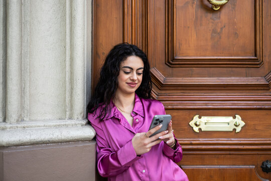 Woman using smartphone by historic doorway in city street